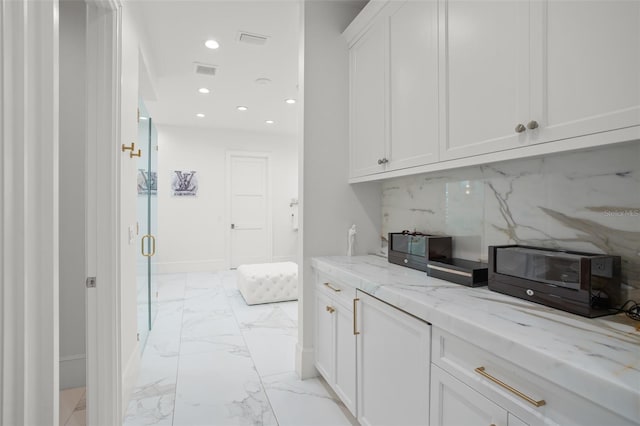 bar with light stone counters, white cabinets, and decorative backsplash