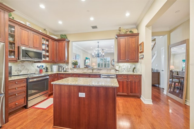 kitchen with ornamental molding, stainless steel appliances, a center island, light stone countertops, and light hardwood / wood-style floors