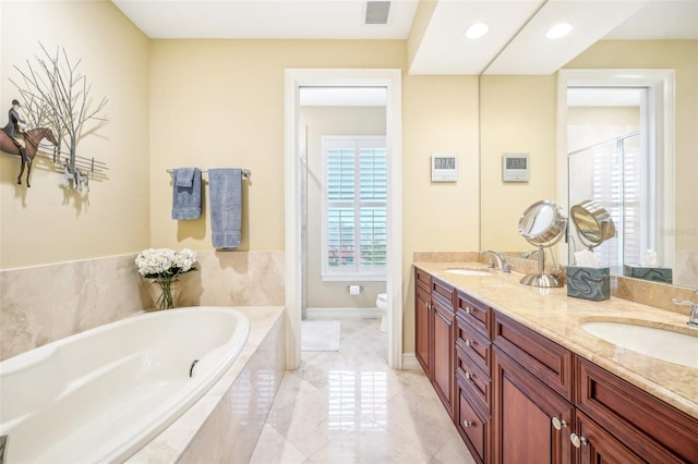 bathroom with tiled bath, vanity, and toilet