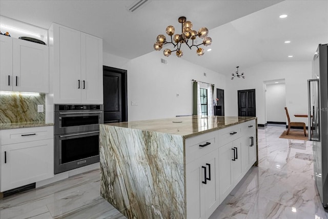 kitchen featuring an inviting chandelier, appliances with stainless steel finishes, light stone counters, a kitchen island, and decorative backsplash