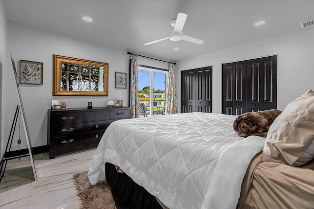 bedroom featuring ceiling fan, light hardwood / wood-style floors, multiple closets, and a textured ceiling