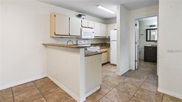 kitchen featuring white cabinets, dark stone countertops, light tile patterned floors, white appliances, and kitchen peninsula