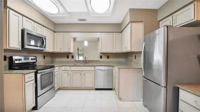 kitchen with light tile patterned flooring, cream cabinets, stainless steel appliances, and sink