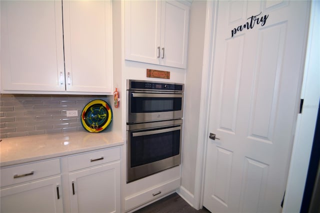 kitchen with stainless steel double oven, backsplash, dark hardwood / wood-style flooring, light stone counters, and white cabinets