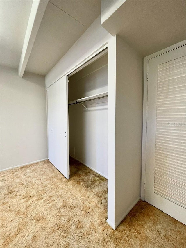 unfurnished bedroom featuring beam ceiling, carpet flooring, and a closet