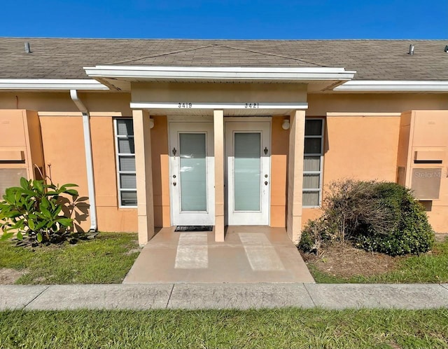 doorway to property with a shingled roof and stucco siding