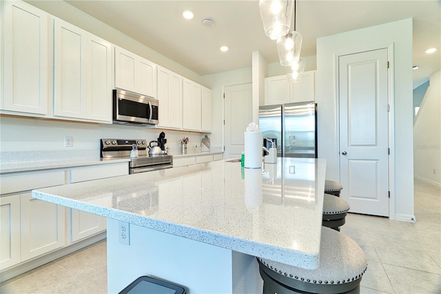 kitchen with decorative light fixtures, stainless steel appliances, a kitchen island with sink, and white cabinetry