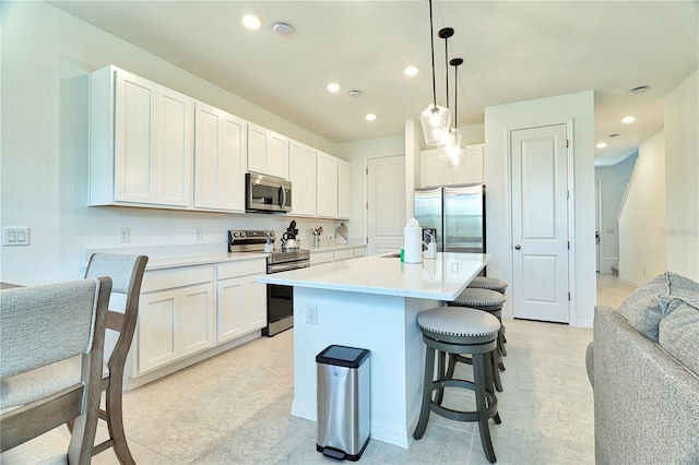 kitchen featuring a kitchen island with sink, white cabinetry, decorative light fixtures, stainless steel appliances, and a breakfast bar area