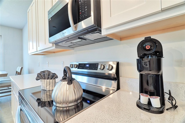 kitchen featuring stainless steel appliances, light stone counters, and white cabinets