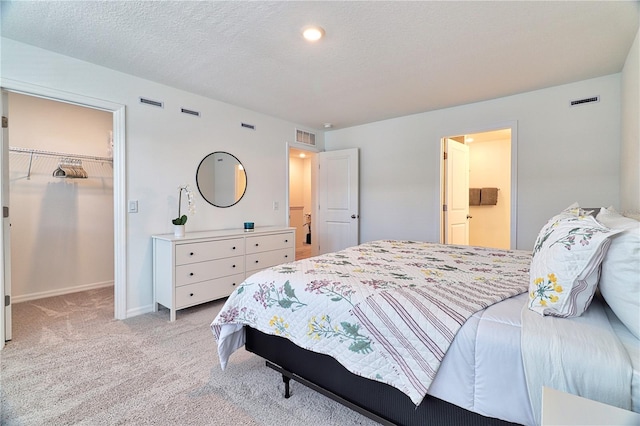 bedroom featuring a walk in closet, a closet, light carpet, and a textured ceiling