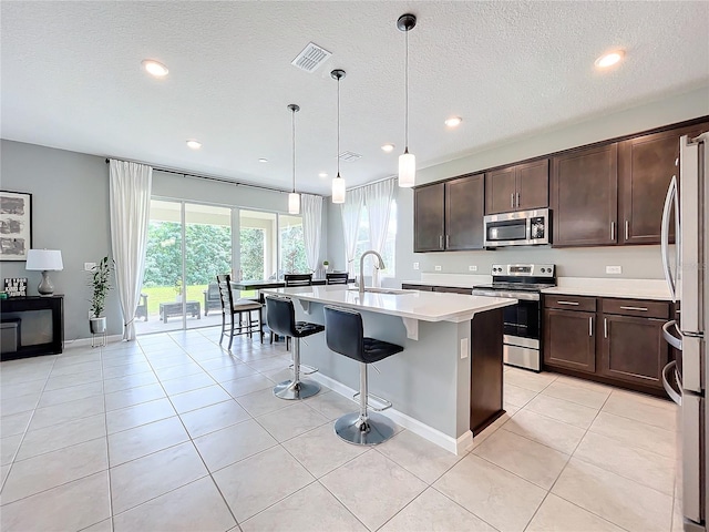 kitchen featuring stainless steel appliances, sink, hanging light fixtures, a kitchen island with sink, and light tile patterned flooring