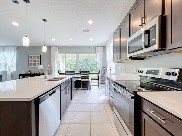 kitchen featuring a center island with sink, sink, light tile patterned flooring, hanging light fixtures, and appliances with stainless steel finishes