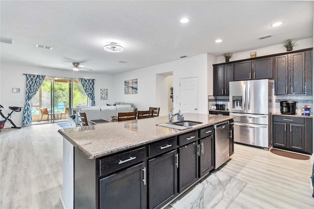 kitchen featuring light stone counters, stainless steel appliances, sink, an island with sink, and ceiling fan