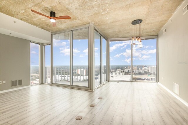 unfurnished room featuring light wood-type flooring, ceiling fan with notable chandelier, and a wall of windows