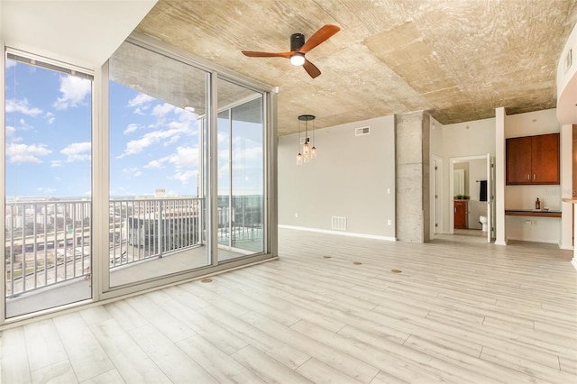 unfurnished living room featuring light wood-type flooring, ceiling fan with notable chandelier, and a wall of windows