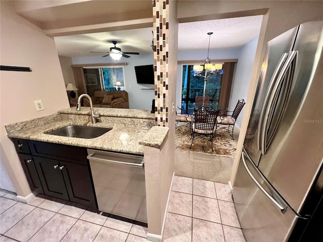 kitchen with a textured ceiling, ceiling fan with notable chandelier, pendant lighting, stainless steel appliances, and sink