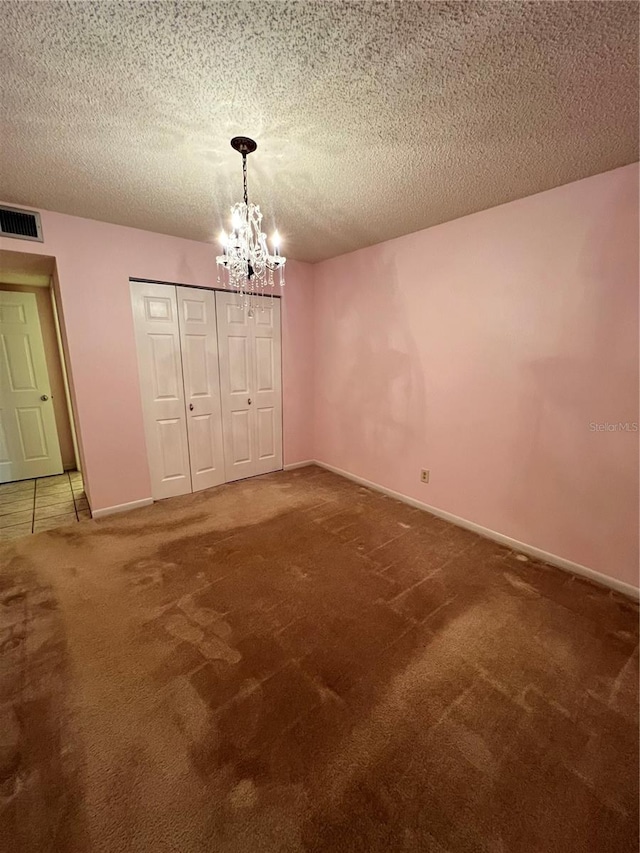 unfurnished bedroom featuring a closet, a textured ceiling, a notable chandelier, and carpet floors