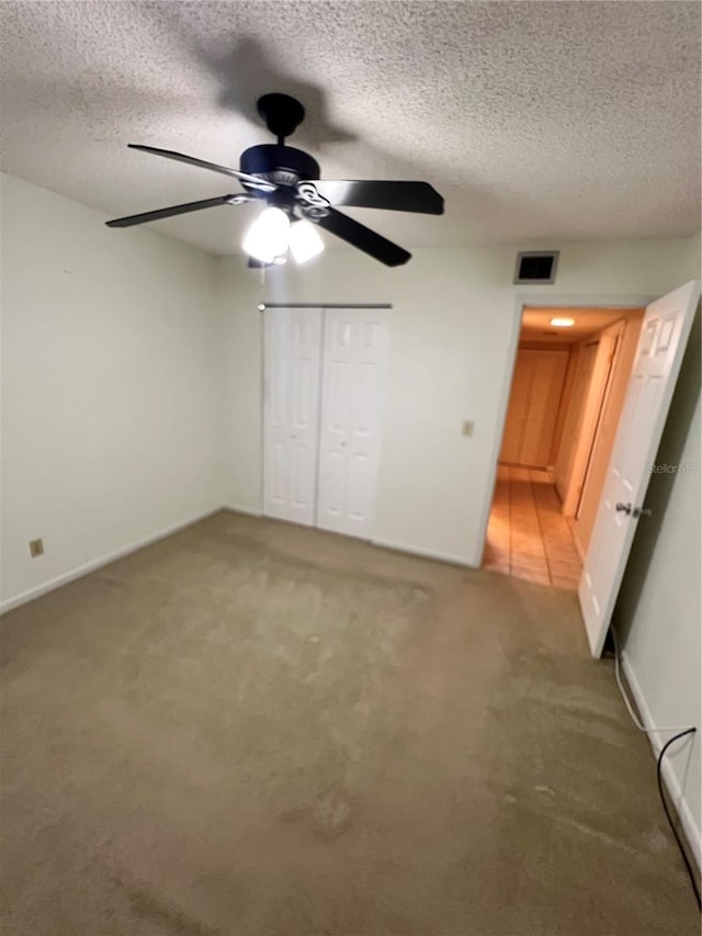 unfurnished bedroom with a textured ceiling, carpet flooring, ceiling fan, and a closet