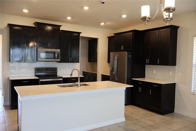 kitchen featuring backsplash, appliances with stainless steel finishes, an island with sink, sink, and a chandelier