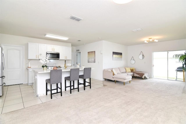 kitchen with a breakfast bar, light carpet, a center island with sink, white cabinetry, and stainless steel appliances