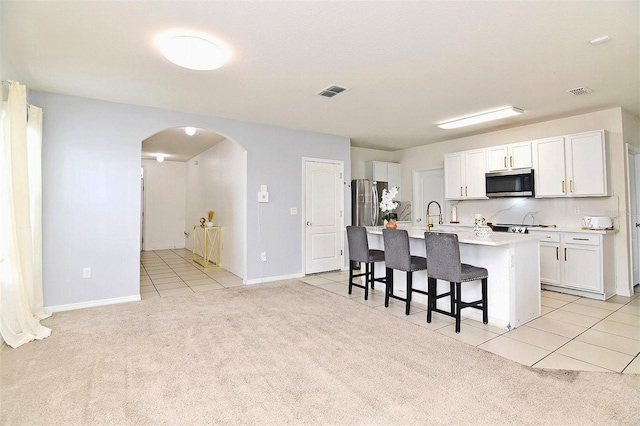 kitchen featuring light carpet, appliances with stainless steel finishes, a center island with sink, and white cabinetry