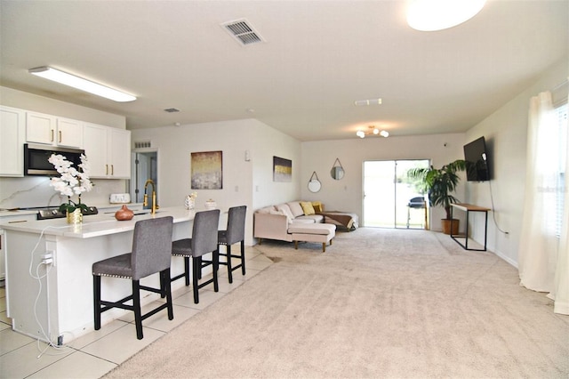 kitchen featuring light carpet, a center island with sink, sink, a kitchen bar, and white cabinetry