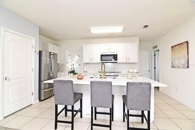 kitchen with a breakfast bar, appliances with stainless steel finishes, white cabinetry, and a kitchen island with sink