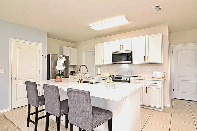 kitchen with a center island with sink, white cabinets, sink, appliances with stainless steel finishes, and light tile patterned flooring