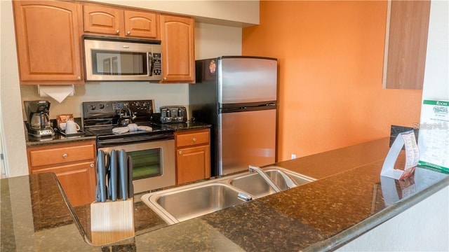 kitchen with dark stone countertops, appliances with stainless steel finishes, kitchen peninsula, and sink