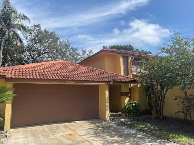 mediterranean / spanish house featuring a tile roof, an attached garage, driveway, and stucco siding