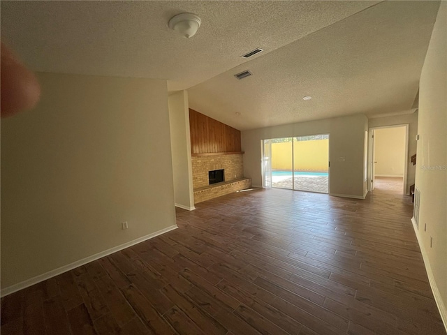 unfurnished living room with a fireplace, vaulted ceiling, a textured ceiling, and dark wood-type flooring