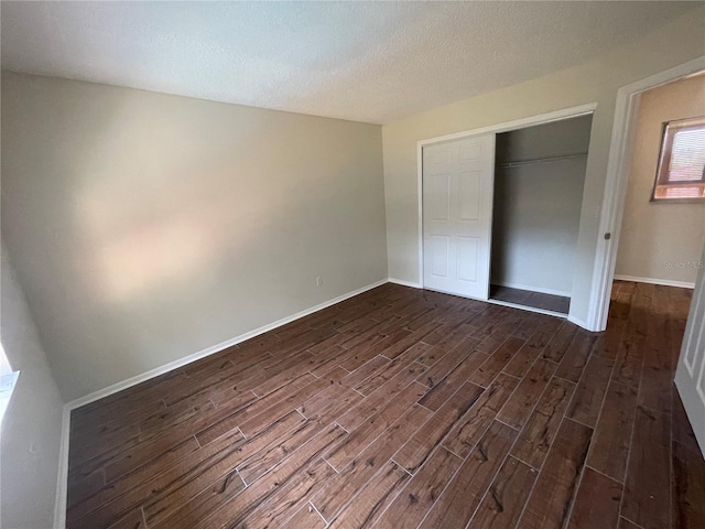 unfurnished bedroom with a textured ceiling, dark hardwood / wood-style flooring, and a closet