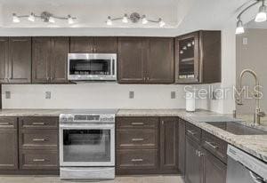 kitchen featuring dark brown cabinetry, stainless steel appliances, light stone counters, and sink