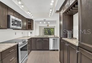 kitchen featuring light stone counters, stainless steel appliances, wood-type flooring, track lighting, and dark brown cabinetry