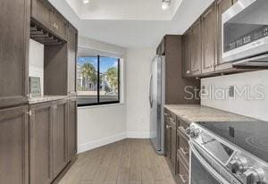 kitchen with light wood-type flooring, light stone counters, and stainless steel range