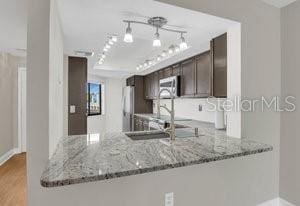 kitchen featuring light hardwood / wood-style floors, dark brown cabinets, kitchen peninsula, and light stone countertops