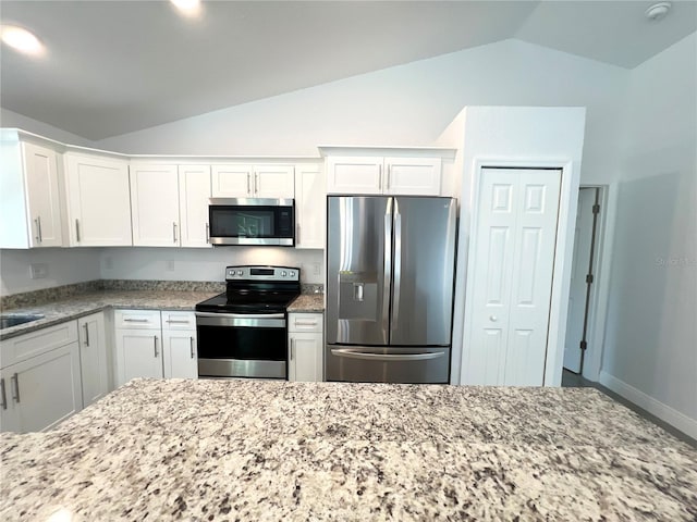 kitchen featuring appliances with stainless steel finishes, vaulted ceiling, light stone countertops, white cabinetry, and baseboards