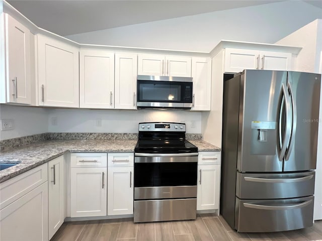 kitchen with white cabinetry, light stone countertops, vaulted ceiling, light hardwood / wood-style floors, and stainless steel appliances