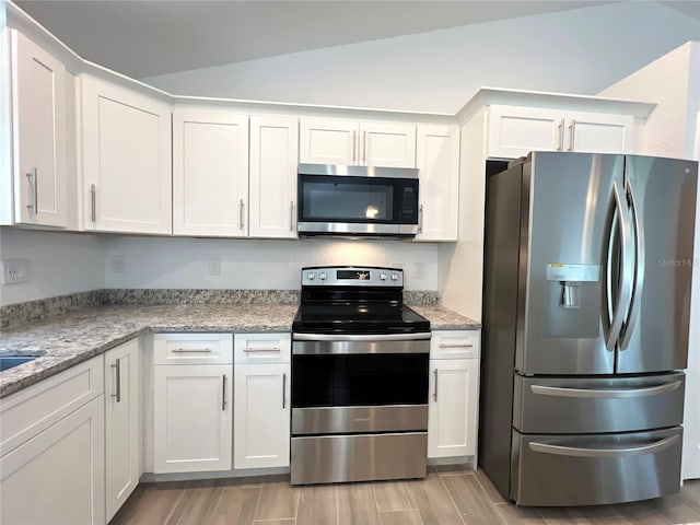 kitchen featuring appliances with stainless steel finishes, wood tiled floors, white cabinets, light stone countertops, and vaulted ceiling