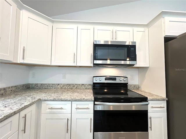 kitchen with white cabinetry, light stone countertops, stainless steel appliances, and vaulted ceiling