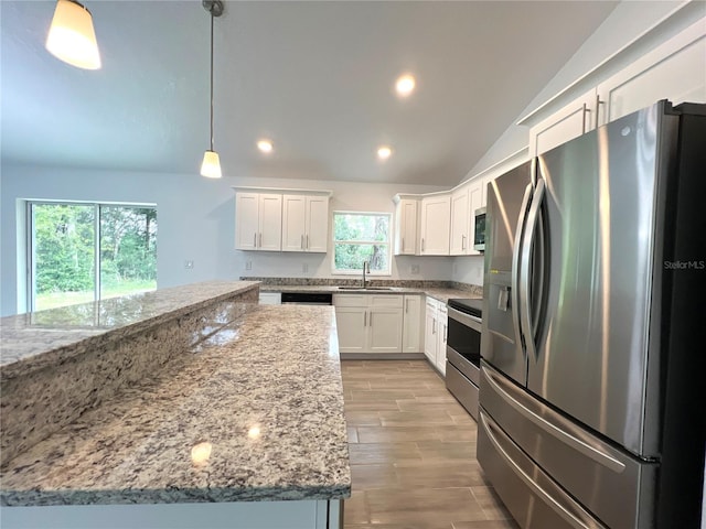 kitchen with appliances with stainless steel finishes, sink, hanging light fixtures, white cabinetry, and vaulted ceiling