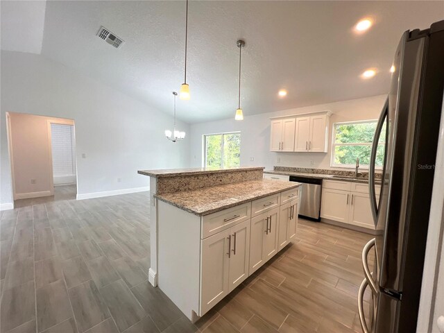 kitchen featuring appliances with stainless steel finishes, plenty of natural light, white cabinetry, lofted ceiling, and pendant lighting