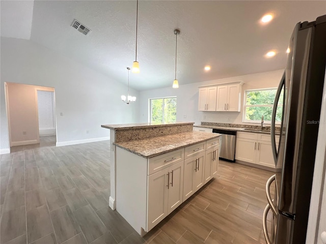 kitchen featuring stainless steel appliances, vaulted ceiling, wood tiled floors, a kitchen island, and white cabinetry