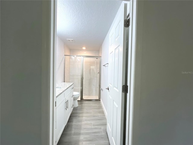 full bath with a textured ceiling, a stall shower, toilet, vanity, and wood finished floors