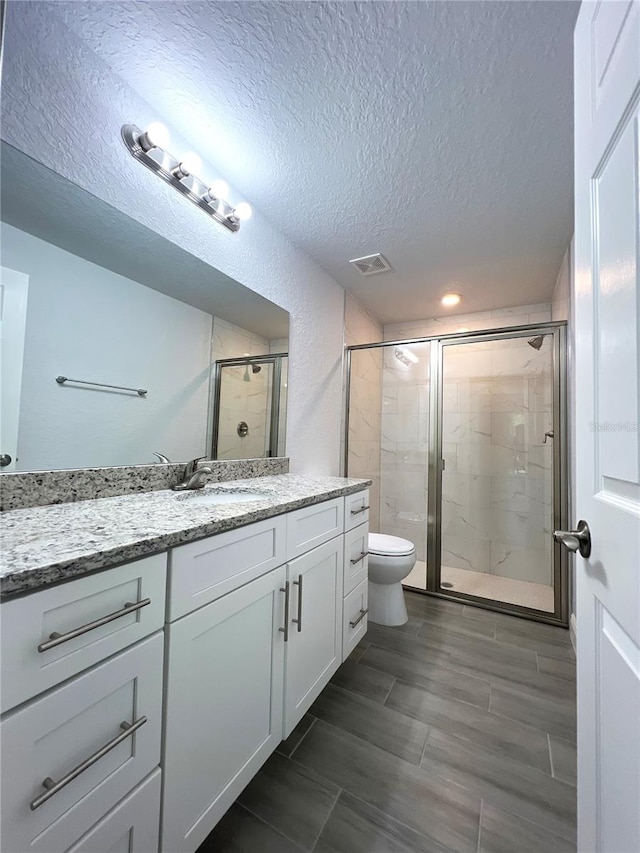 bathroom featuring vanity, toilet, a textured ceiling, and a shower with door