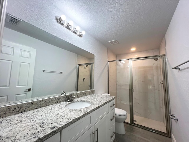 bathroom with a shower stall, a textured ceiling, toilet, vanity, and wood finished floors