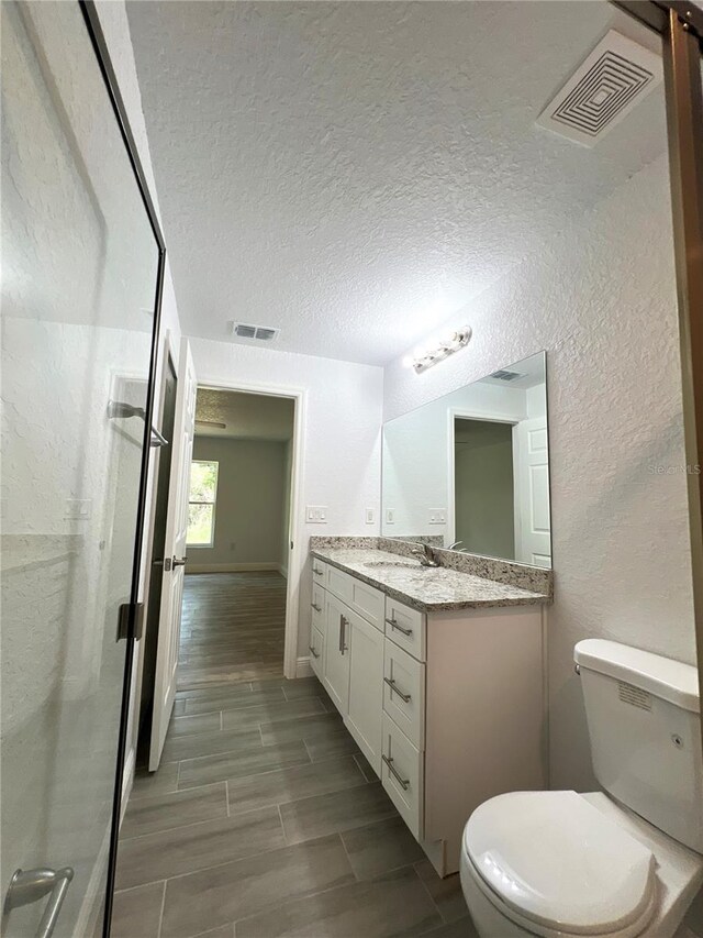 full bath featuring toilet, vanity, a textured ceiling, wood tiled floors, and an enclosed shower