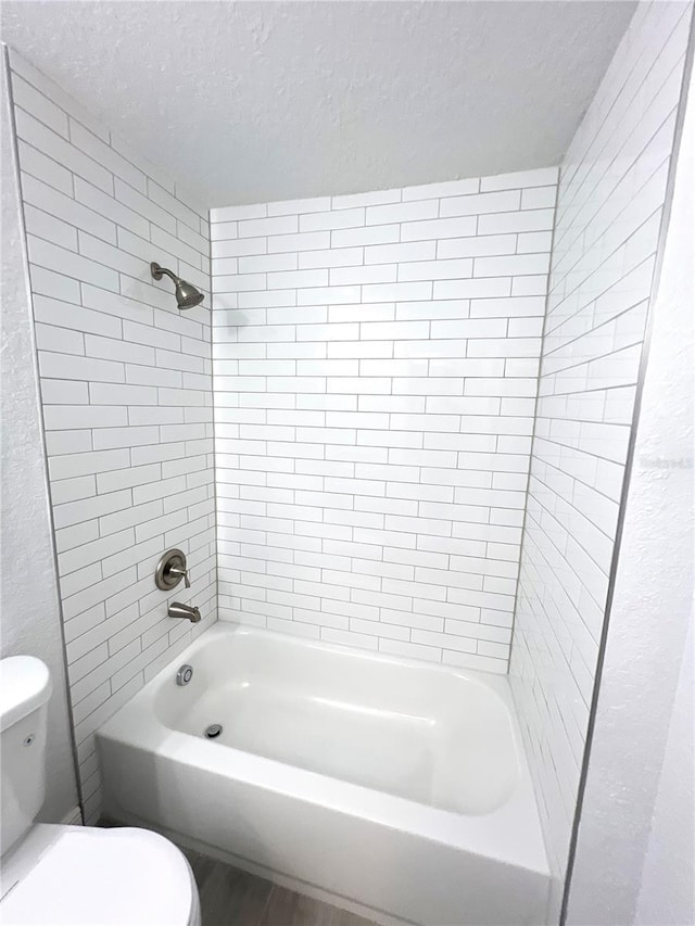 bathroom featuring a textured ceiling, toilet, shower / washtub combination, and wood finished floors