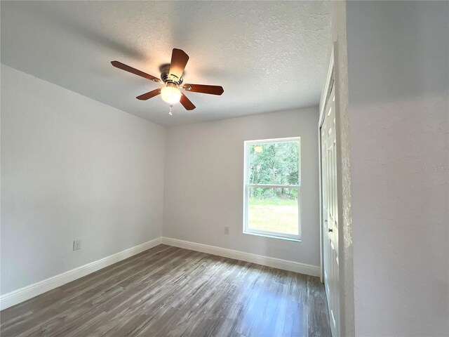 spare room featuring baseboards, dark wood-type flooring, a ceiling fan, and a textured ceiling