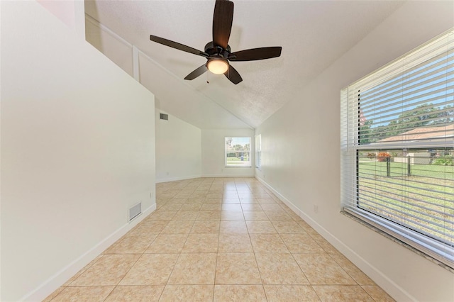 tiled empty room with a textured ceiling, ceiling fan, and vaulted ceiling